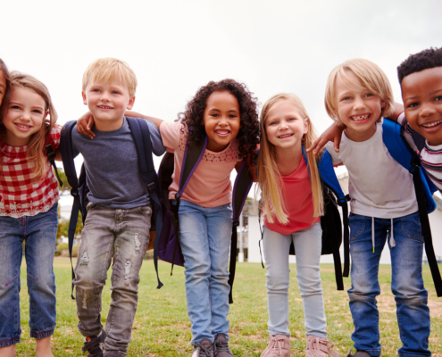 Eine Gruppe von fröhlichen Grundschulkindern legt die Arme umeinander