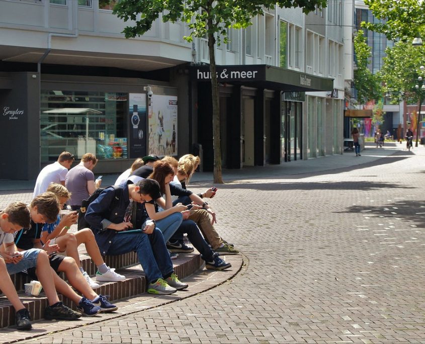 Kinder und Erwachsene sitzen auf einem öffentlichen Platz und starren in ihre Handys